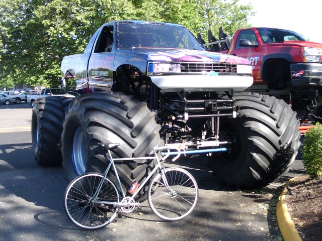 A bicycle resting on the wheel of a monster truck